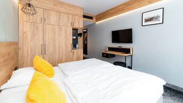 Une chambre d’hôtel moderne équipée d’un lit, d’une armoire en bois, d’un bureau et d’un téléviseur fixé au mur.
