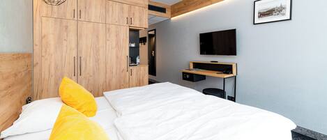 Ein modernes Hotelzimmer mit Bett, Holzschrank, Schreibtisch und einem Wand-Fernseher.