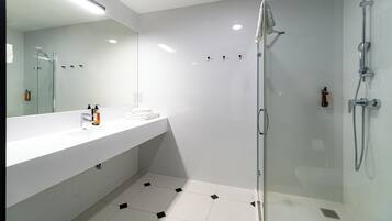 Un baño moderno con cabina de ducha de vidrio, un lavamanos blanco con espejo y suelo de baldosas con diseño geométrico.