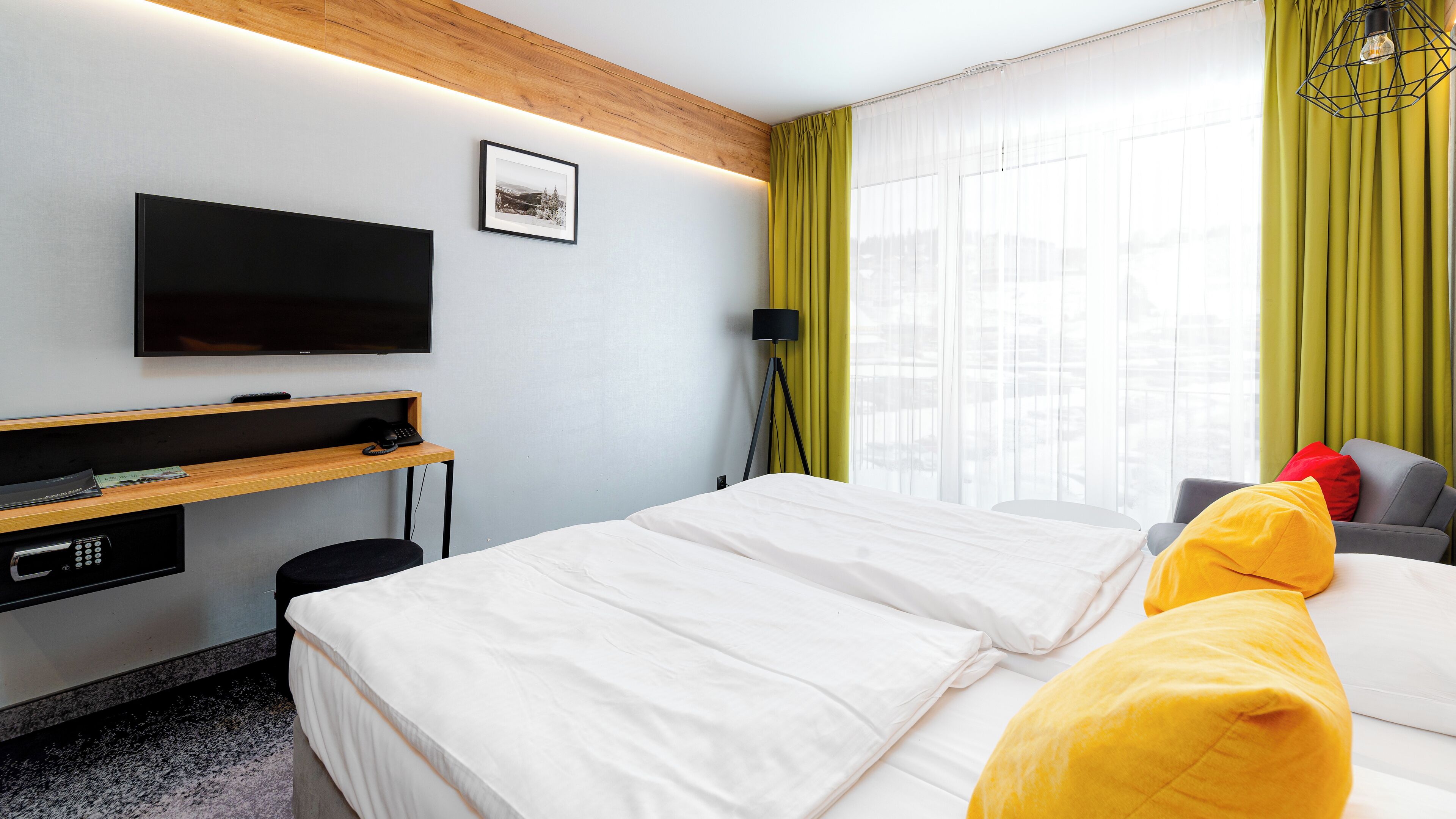 Habitación de hotel con cama, escritorio, televisor de pantalla plana, lámpara y ventana con cortinas.