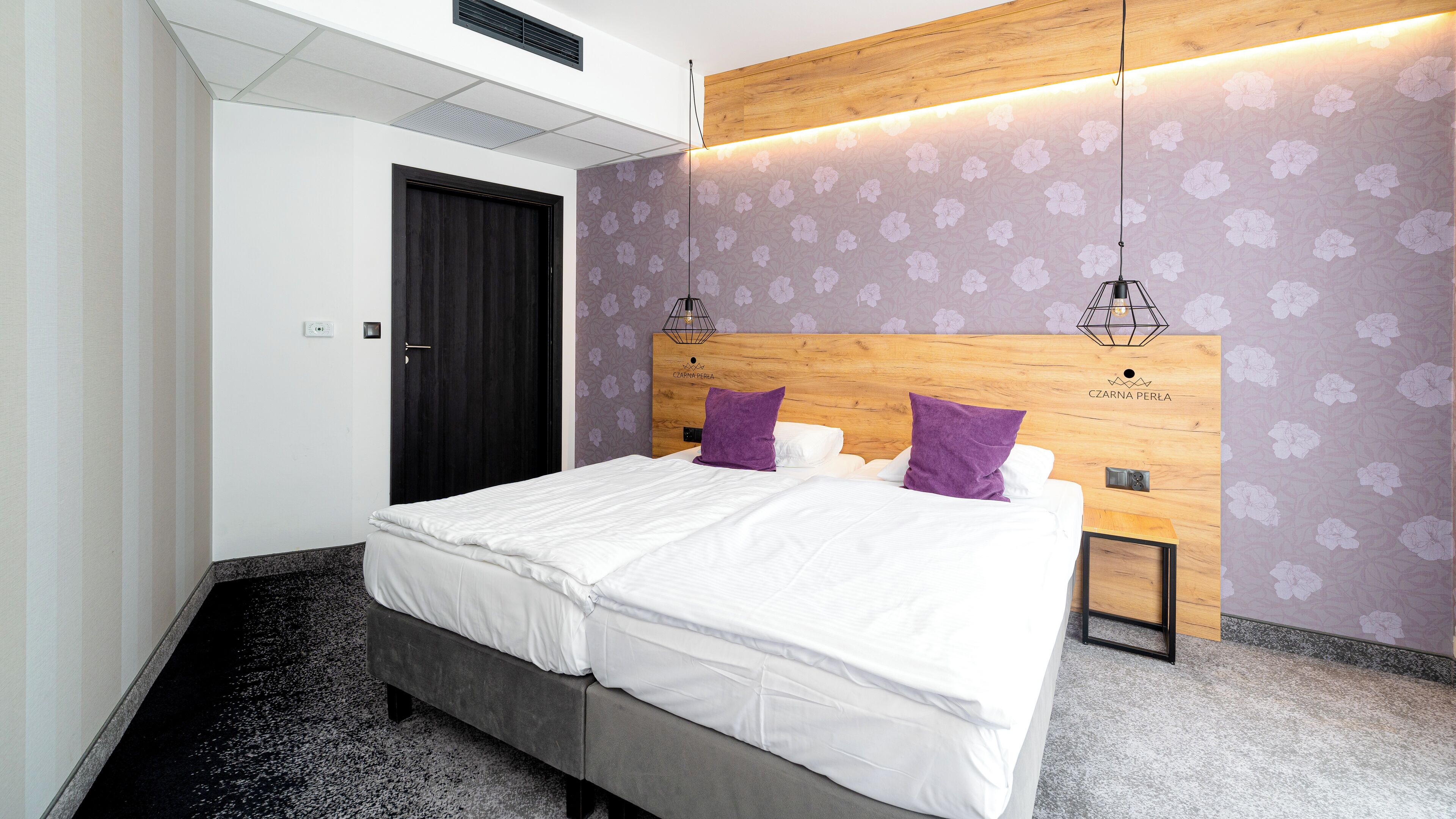 A modern hotel room with a large bed, a wooden headboard, and a floral-patterned wall.