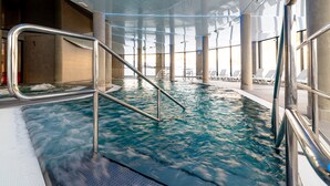 Ein Hallenbad mit klarem Wasser, Metallgeländern und Liegestühlen am Beckenrand.