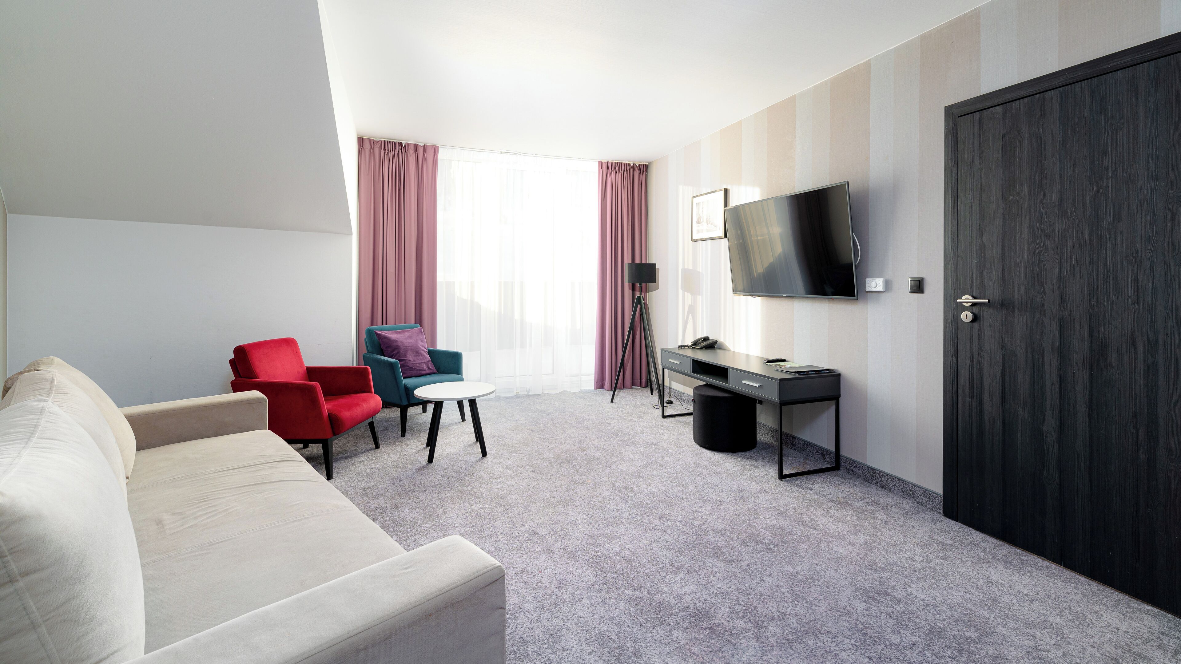 A hotel room with a sofa, two armchairs, a desk, a television, and a wardrobe.