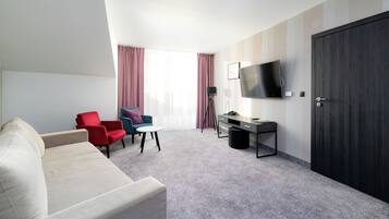 A hotel room with a sofa, two armchairs, a desk, a television, and a wardrobe.