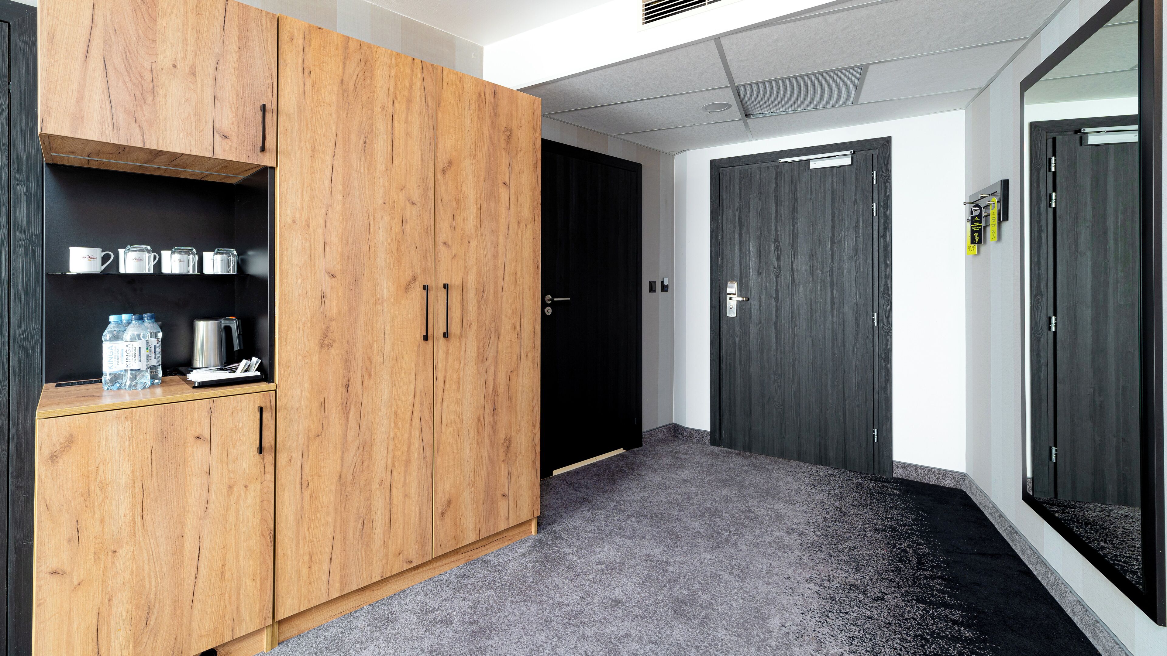 A hallway with a wooden wardrobe, a black door, and a water dispenser on a shelf.