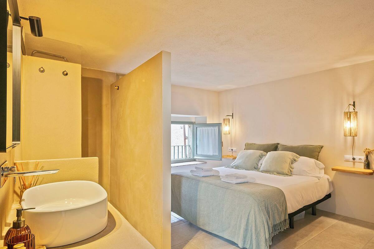 A hotel room with a large bathtub, a bed with pillows, and a bedside table with a lamp.
