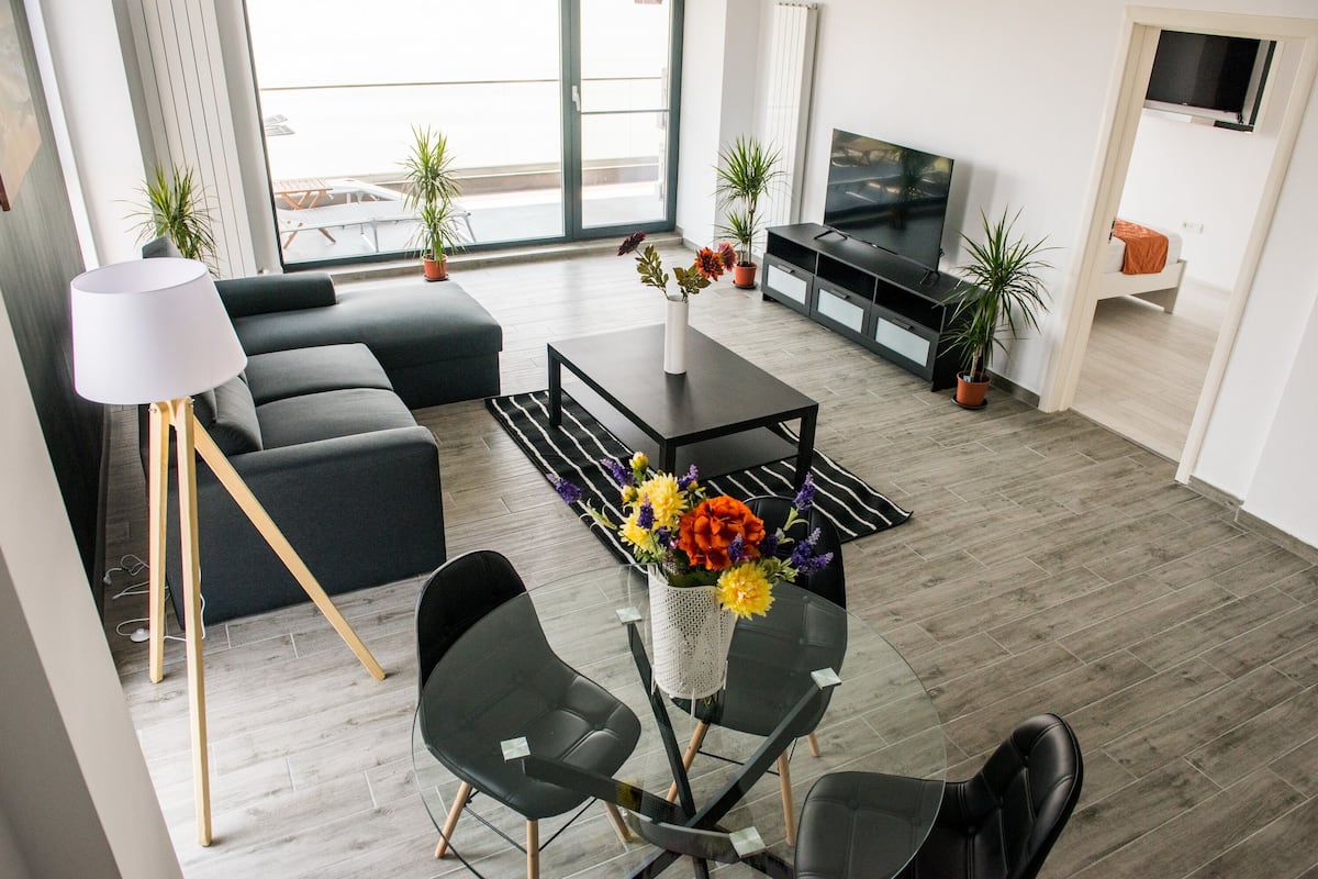 A modern living room with a sofa, coffee table, TV, and potted plants.