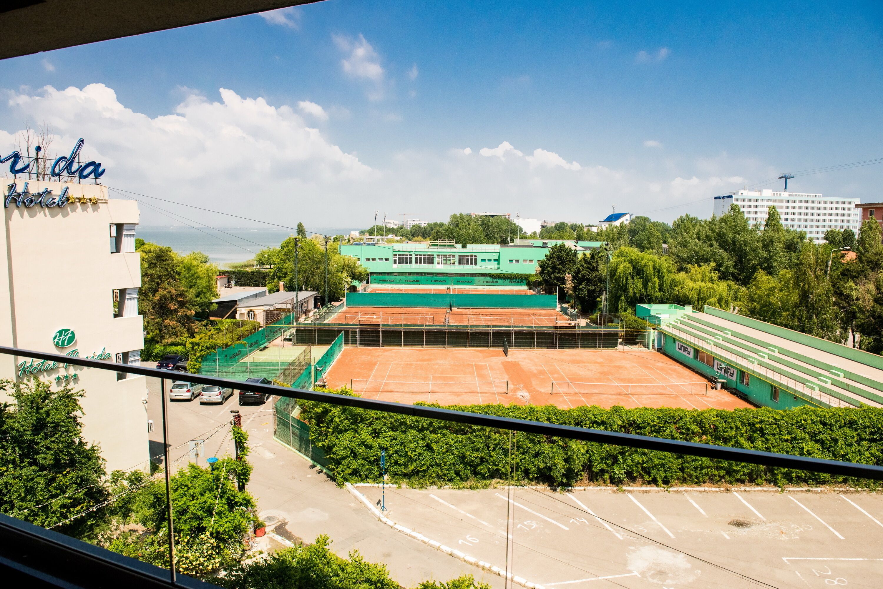 A hotel with a tennis court, a parking lot, and a view of the surrounding buildings.