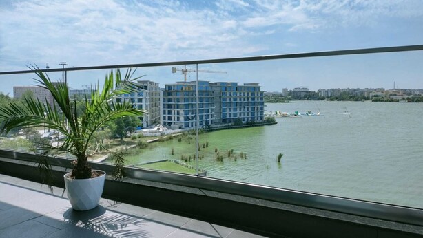 A view from a balcony overlooking a river with modern buildings and a construction crane in the background. - Diamond View Apartments (Constanta)