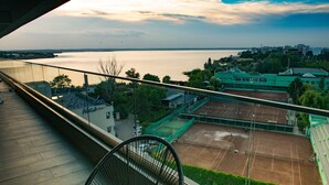 A balcony with a tennis court view, a chair, and a building with a green roof. - Diamond View Apartments (Constanta)