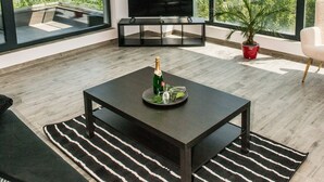 A modern living room with a large TV, a coffee table with a bottle, and a potted plant. - Diamond View Apartments (Constanta)