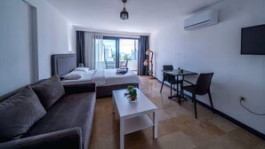 A modern hotel room with a bed, a sofa, a small table, a desk, and a TV. - Ilya Apart 2  (Bodrum)