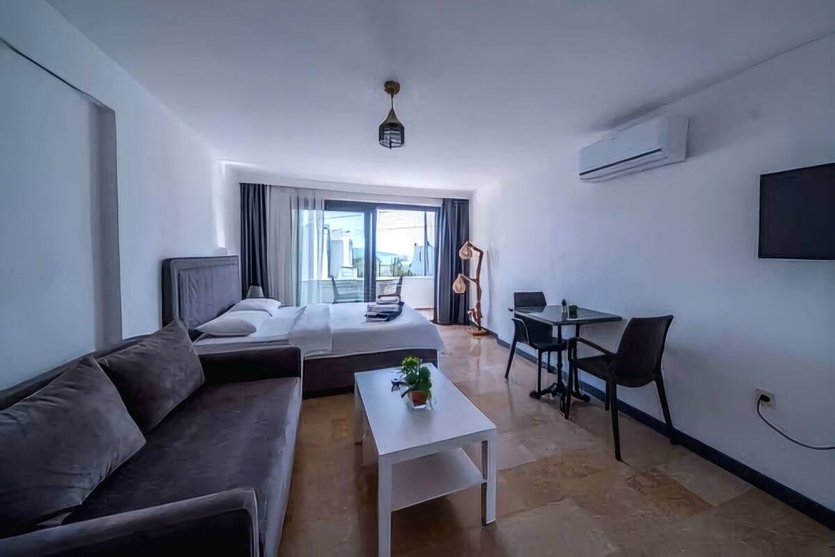 A modern hotel room with a bed, a sofa, a small table, a desk, and a TV.