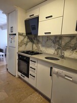 Una cocina moderna con armarios blancos, protector contra salpicaduras de mármol, horno empotrado, lavavajillas y estufa a gas.
