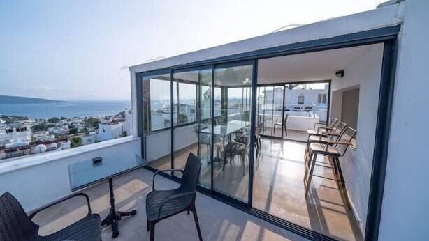 A modern balcony with a glass enclosure, offering a view of the sea and cityscape. - Ilya Apart 2  (Bodrum)
