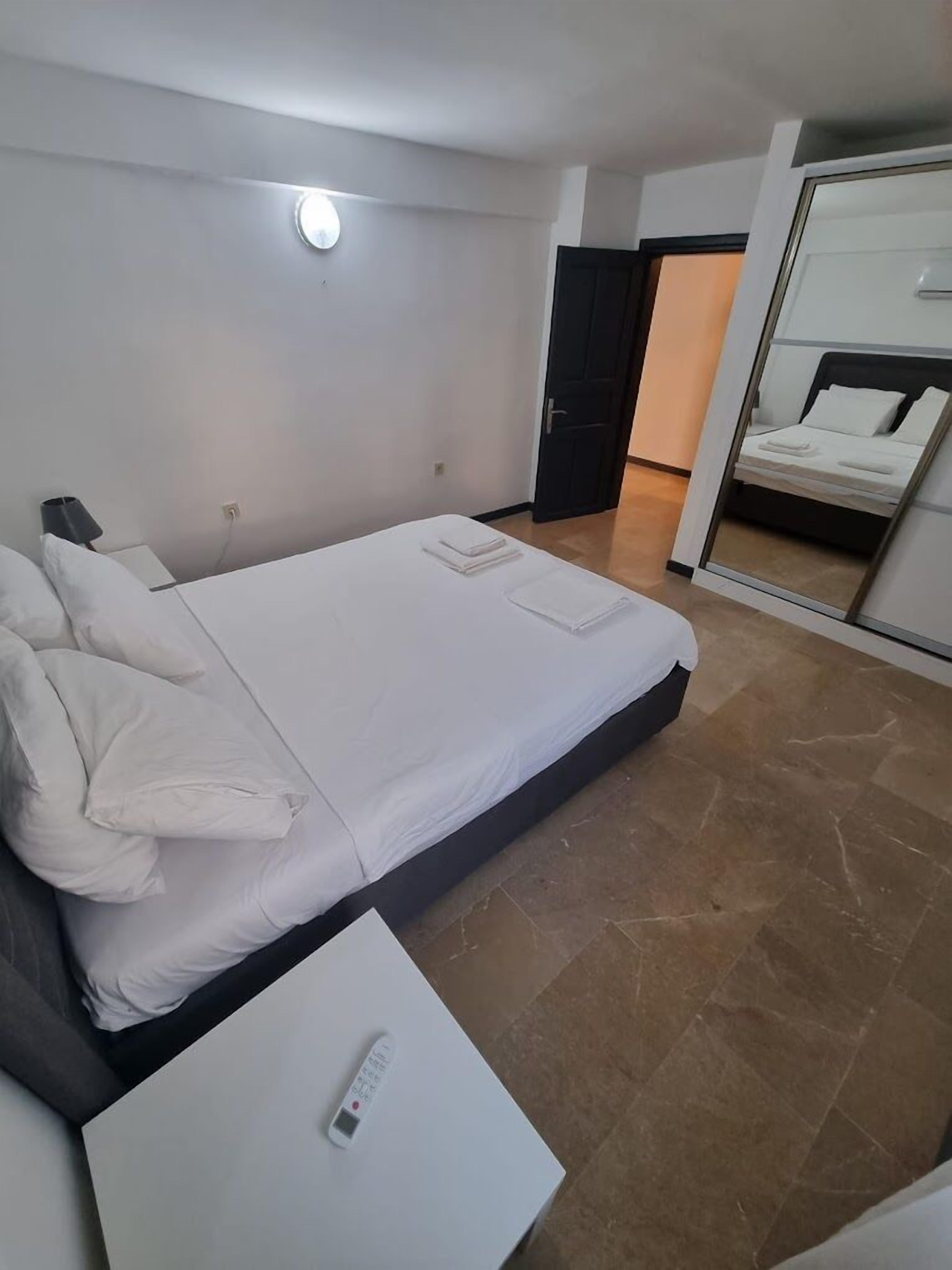 Hotelkamer met een bed, nachtkastje met een afstandsbediening, spiegel en een deur naar een andere kamer.