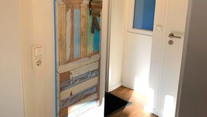 Un pasillo con un adorno de pared de madera, una puerta con ventanal azul y suelo de madera.