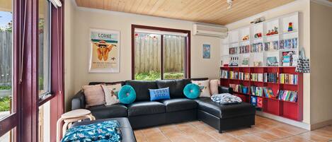 A modern living room with a sectional sofa, a small table, a bookshelf filled with books, and a poster on the wall.