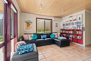 Ein modernes Wohnzimmer mit einem Ecksofa, einem kleinen Tisch, einer Bücherwand voller Bücher und einem Poster an der Wand.