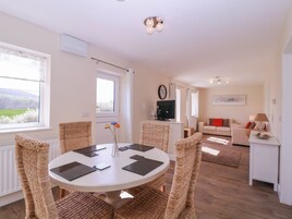 A modern living room with a round dining table, wicker chairs, a sofa, and a television.