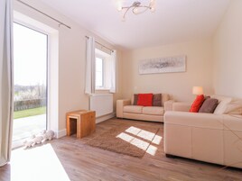 A living room with a sofa, a small wooden table, a lamp, and a view of a garden through a large window.