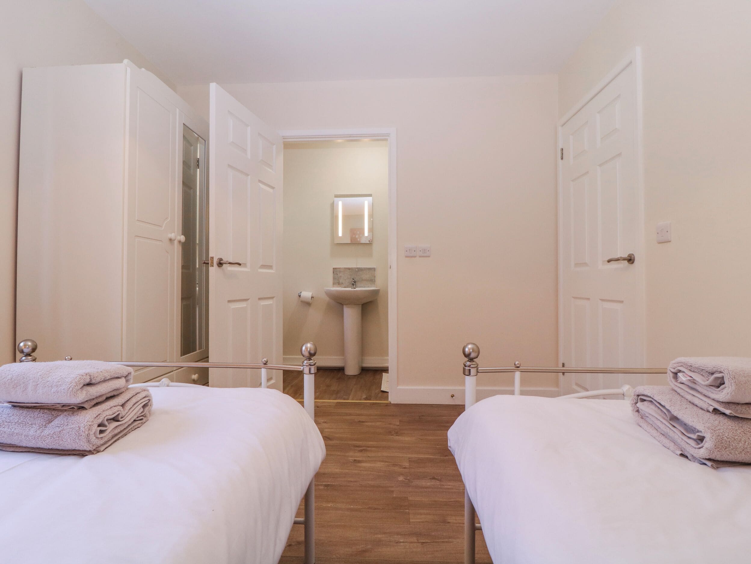 A hotel room with two beds, a bathroom with a sink and mirror, and a hallway leading to another room.
