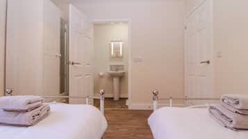A hotel room with two beds, a bathroom with a sink and mirror, and a hallway leading to another room.