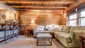 L’intérieur d’un chalet accueillant, avec un plafond en bois, un ensemble de canapés, un coin repas avec des chaises en métal et une petite table.