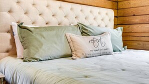 Une chambre à coucher avec une tête de lit capitonnée, un lit recouvert d’une couette de couleur claire et deux oreillers, dont l’un porte le mot « re-treat ».