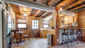 Une cuisine rustique aux murs en bois, avec un grand réfrigérateur, une table à manger entourée de chaises et un coin bar avec des tabourets.