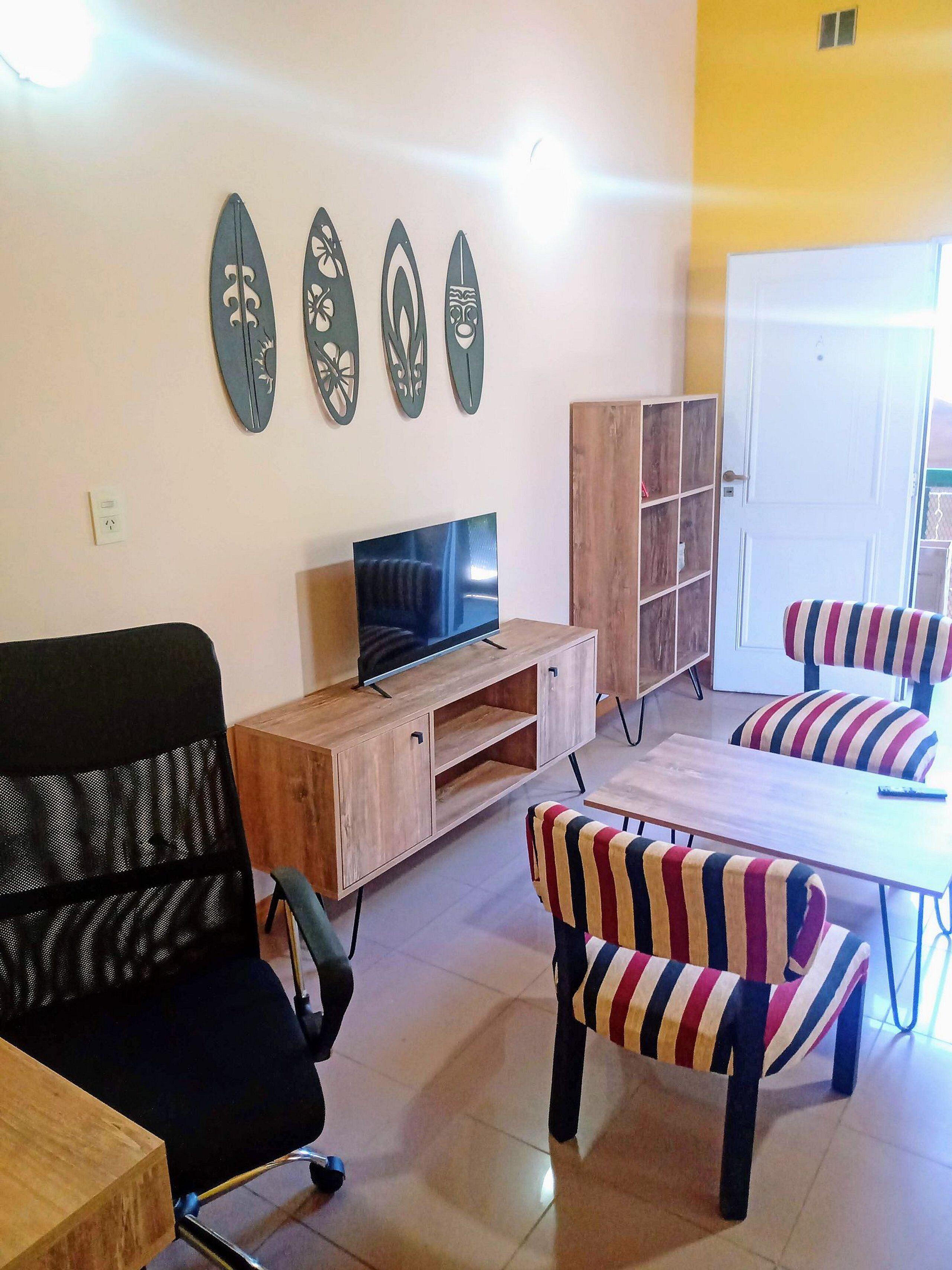 A living room with a TV, wooden furniture, striped chairs, and decorative wall art.