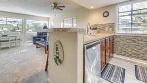 A modern kitchen with a dishwasher, granite countertops, and a dining area with a blue sofa and a table. - Arcadian Dunes 1st-floor Gem: Pool & Beach Access! (Myrtle Beach)