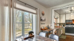 A kitchen with a dining area, wooden cabinets, a stove, and a window with curtains.