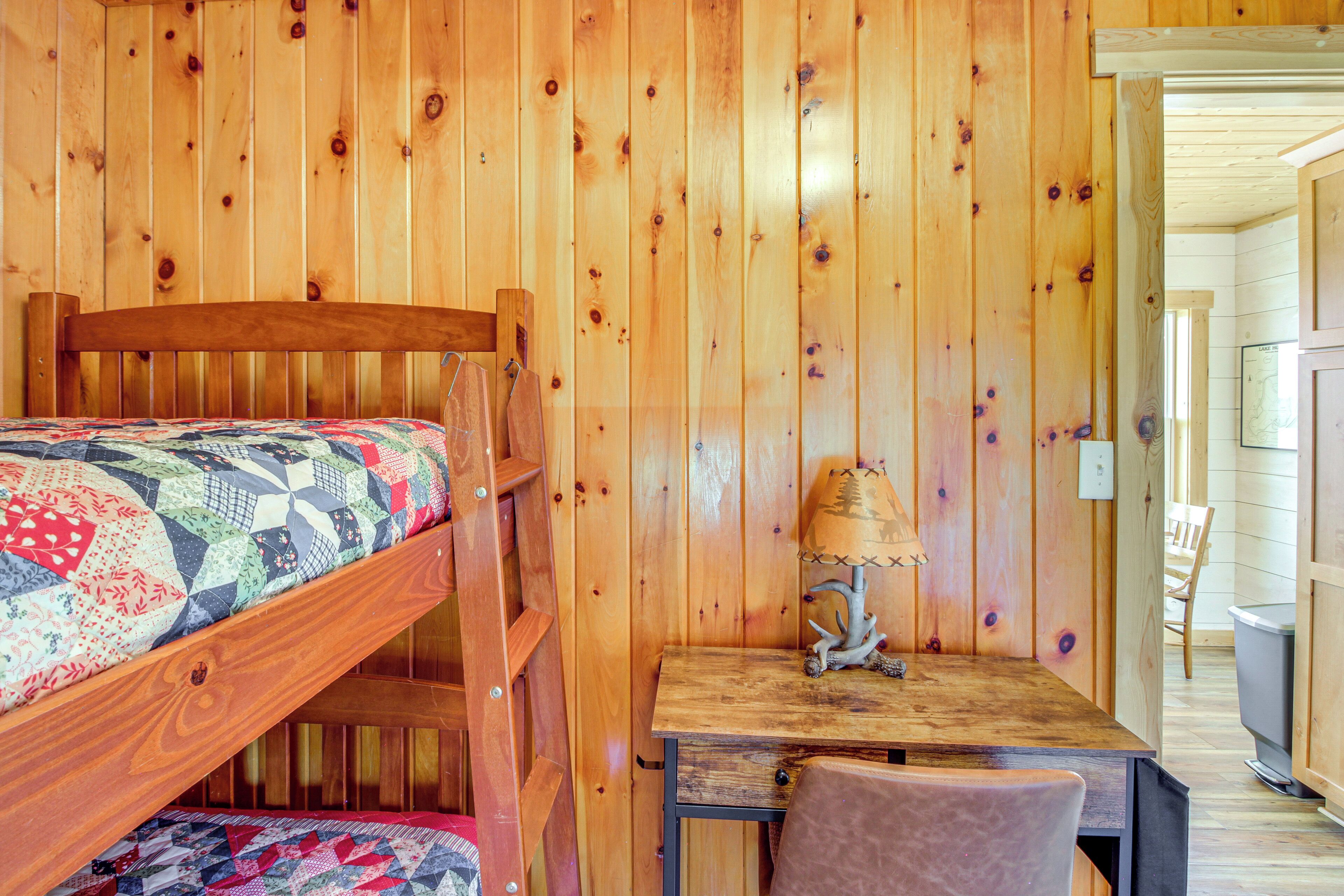 Un letto a castello in legno con copriletto, un tavolino con lampada e una sedia in una stanza con pareti di legno.