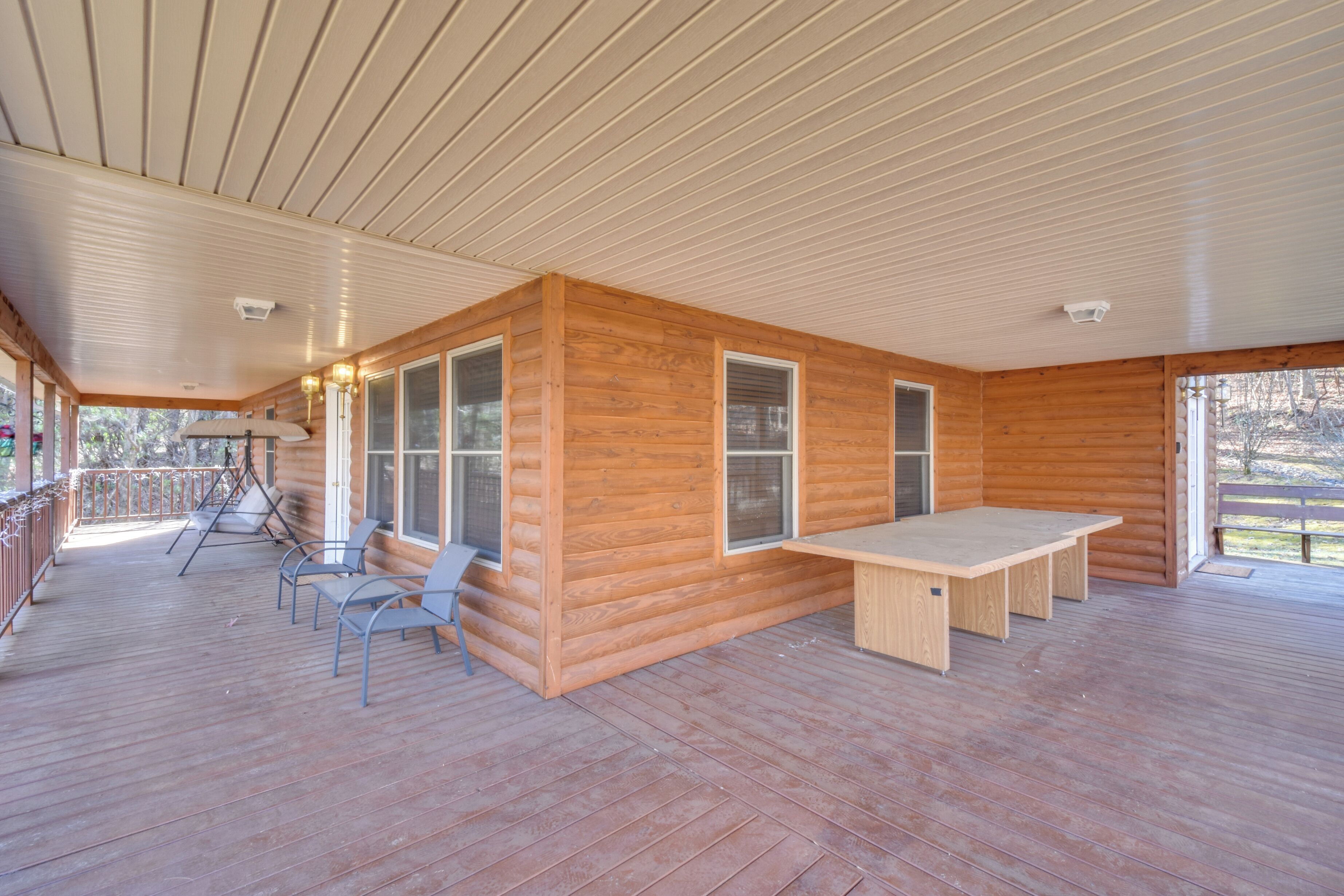 A spacious wooden deck with a table and chairs, large windows, and a covered area with a railing.
