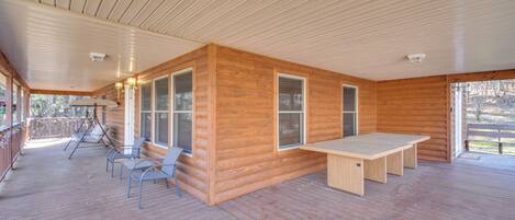 A spacious wooden deck with a table and chairs, large windows, and a covered area with a railing.