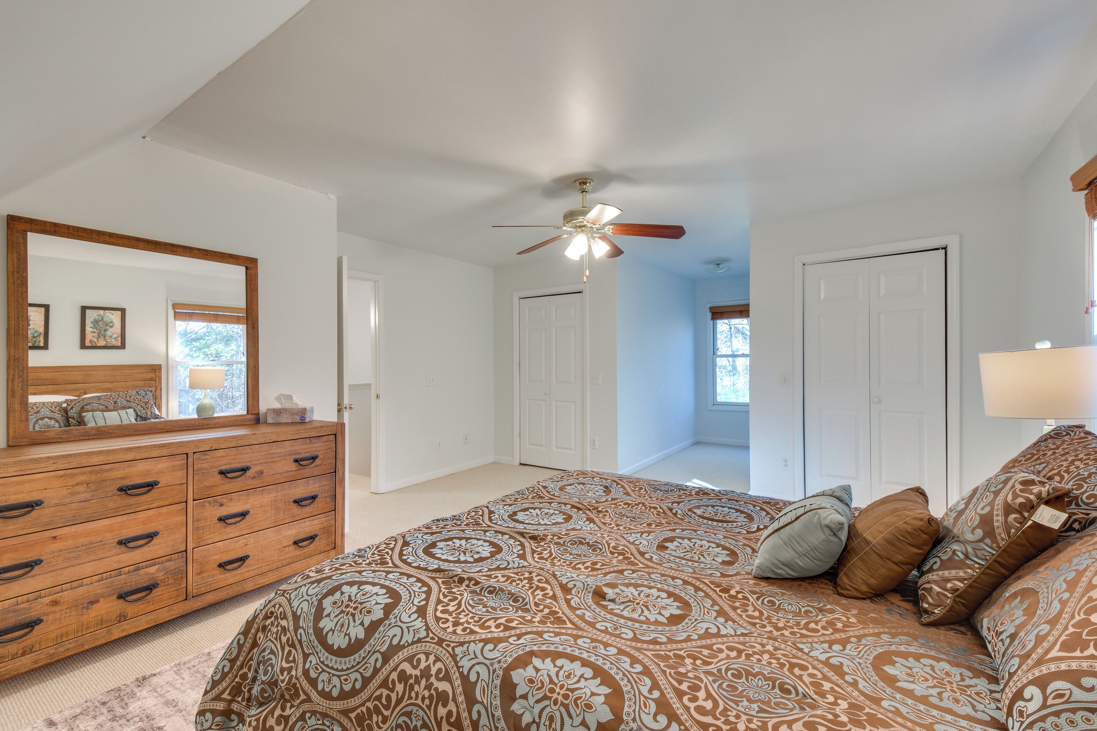 A bedroom with a large bed, a wooden dresser, a ceiling fan, and a view of a hallway.