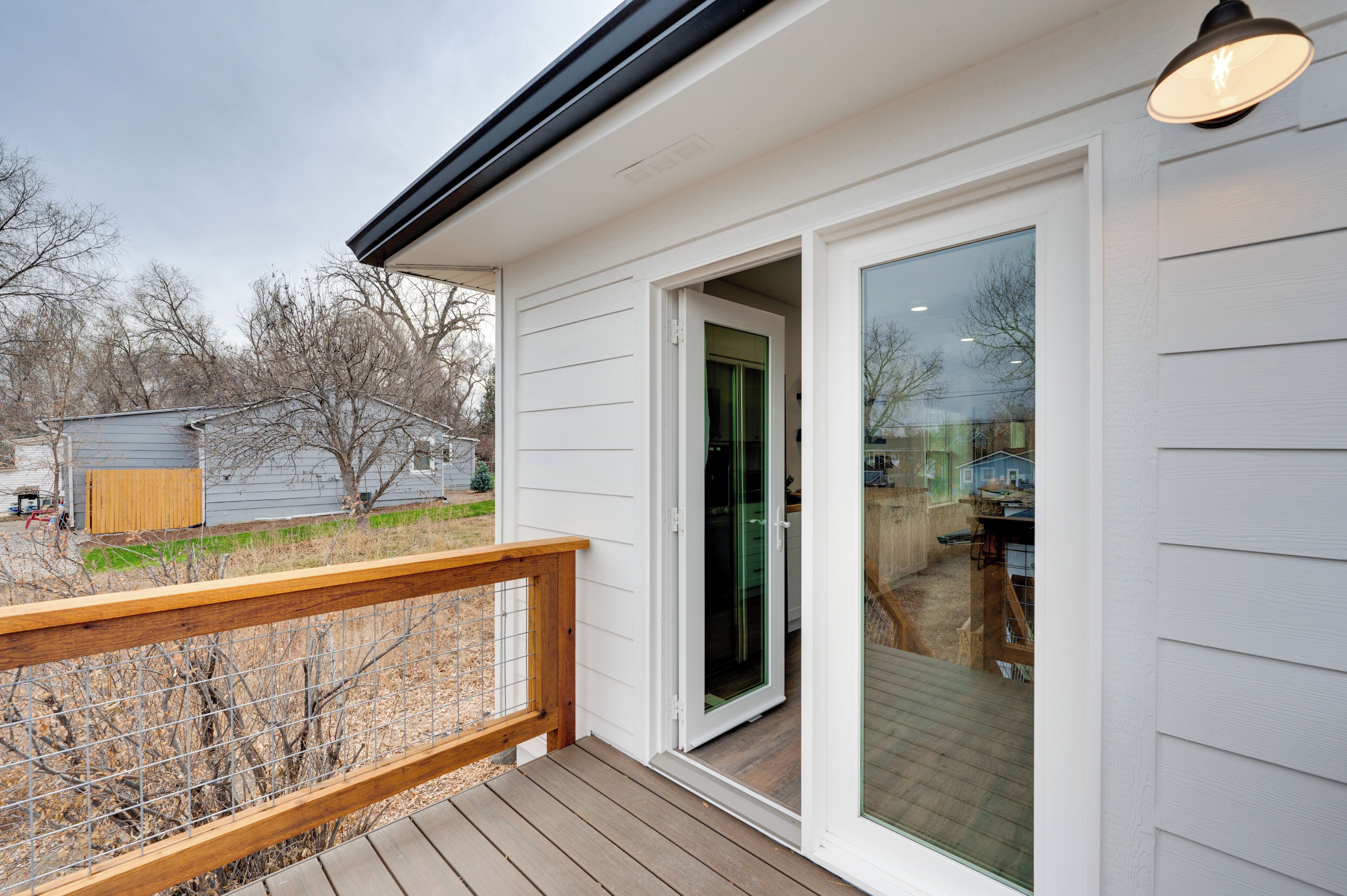 Eine überdachte Terrasse mit Holzgeländer, eine Schiebetür zu einer Garage und eine Leuchte über der Tür.
