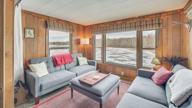 A cozy living room with a grey sofa, a red throw blanket, and a wooden floor. - Mason Cabin w/ Private Dock on Marengo Lake! (Mason)