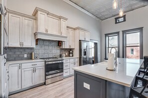 A modern kitchen with light wood cabinets, a central island, stainless steel appliances, and a patterned backsplash.