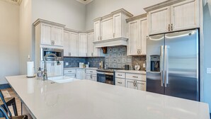 A modern kitchen with white cabinetry, stainless steel appliances, and a large island. - Florence Vacation Rental w/ Rooftop Deck! (Florence)