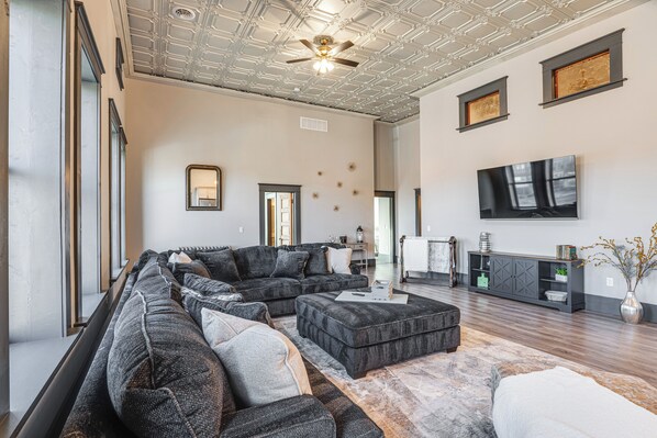 A spacious living room with a sectional sofa, a coffee table, and a flat-screen TV mounted on the wall.