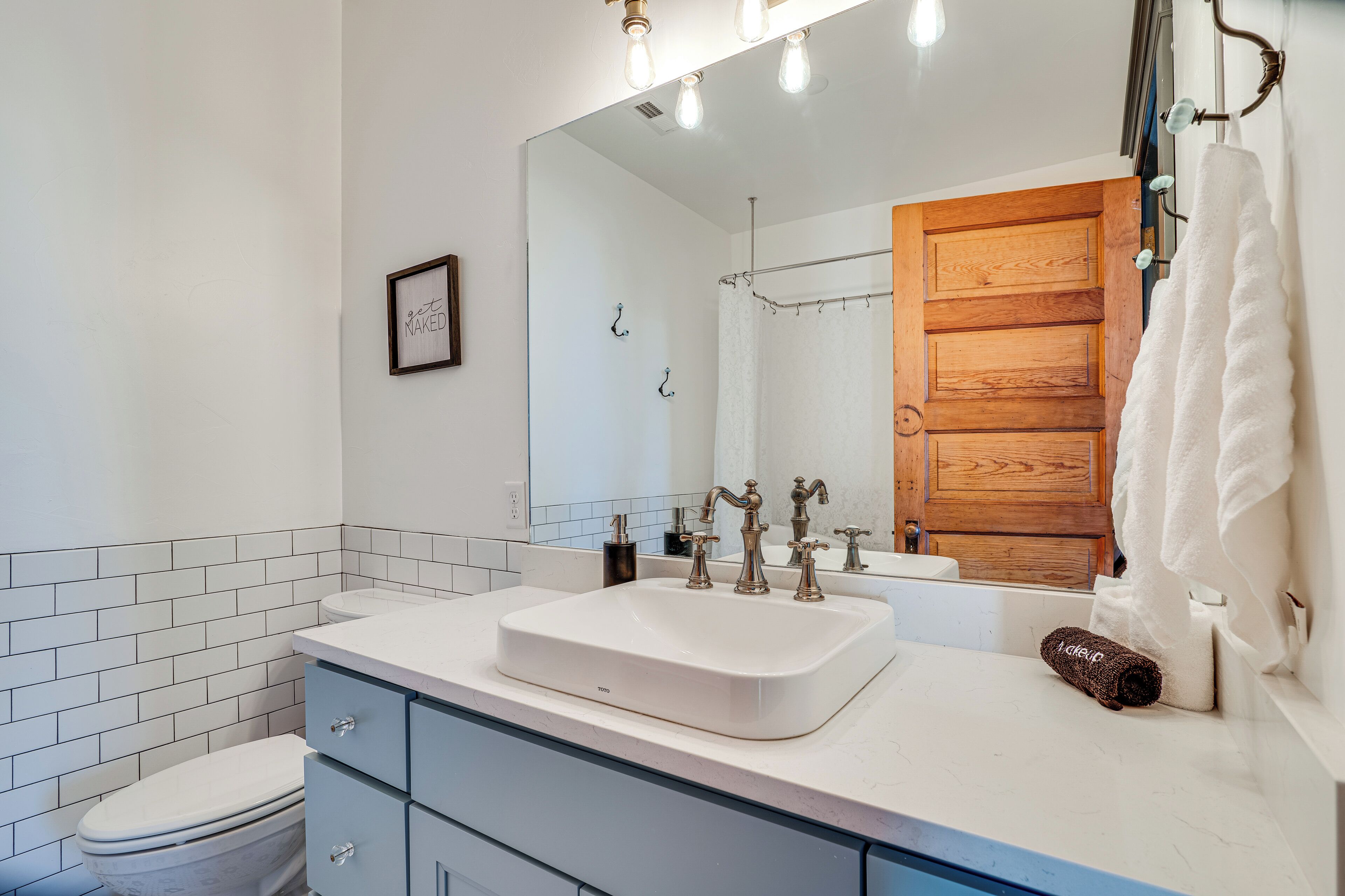 A modern bathroom with a white sink, a wooden door, and a mirror with lights.