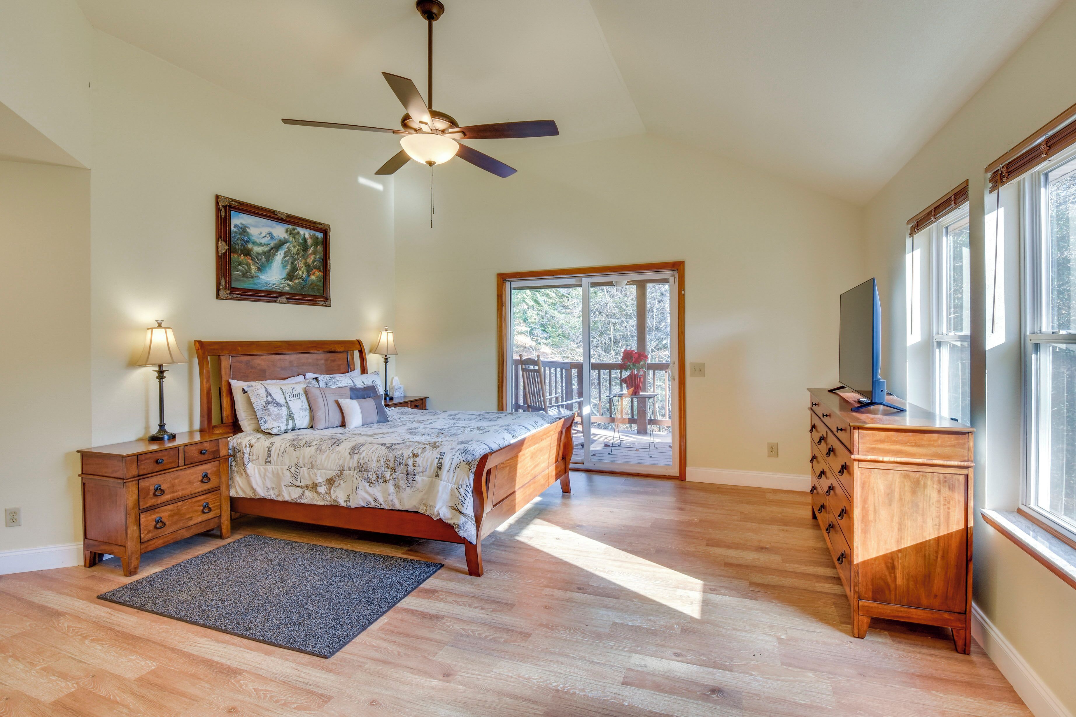 A bedroom with a bed, wooden dresser, ceiling fan, and a large window.