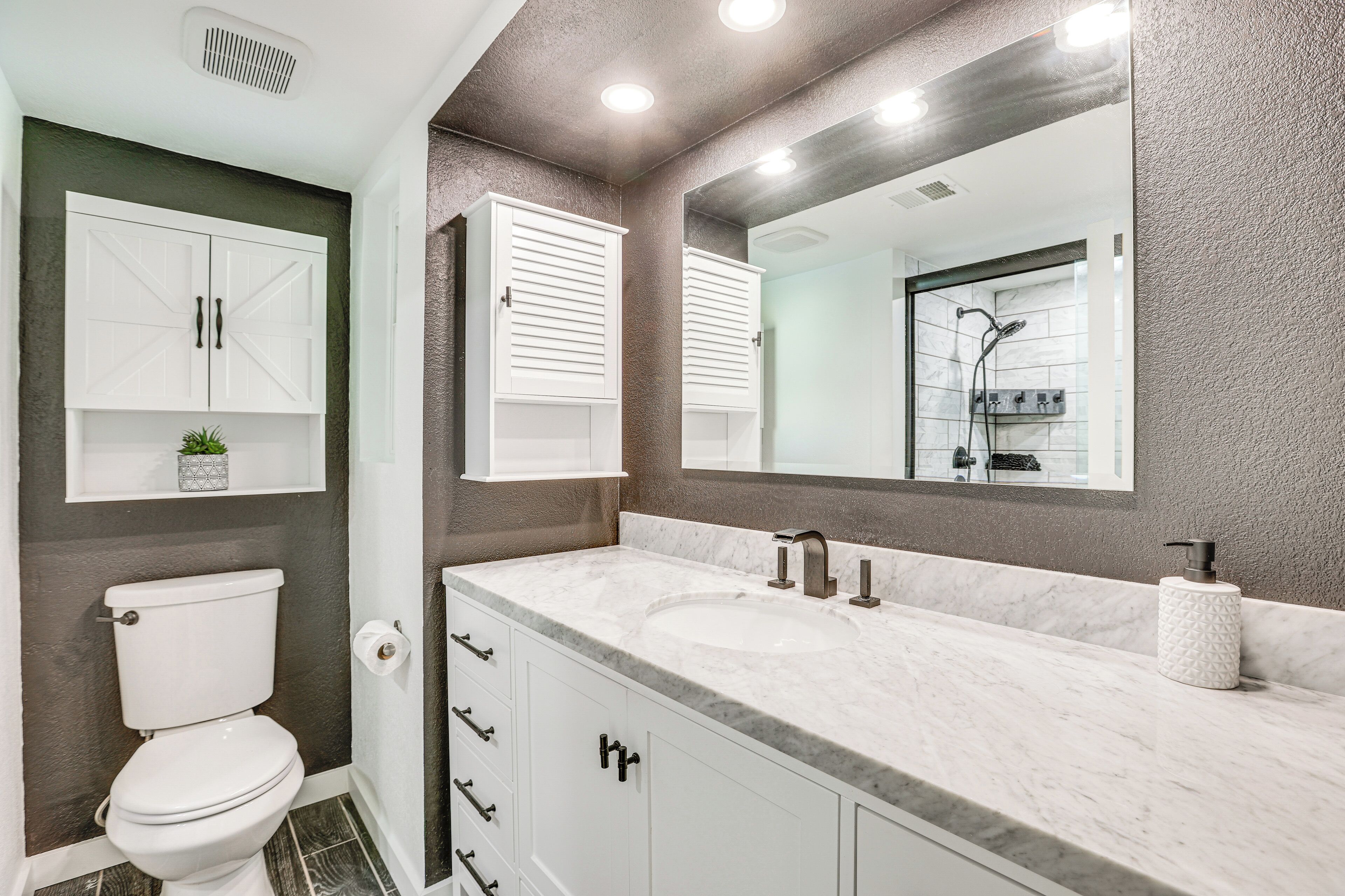 A bathroom with a white toilet, a marble sink, and a large mirror.
