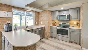 A modern kitchen with a large island, stainless steel appliances, and a brick accent wall. - Peoria Home w/ Private Pool, Hot Tub, & Gas Grill! (Peoria)