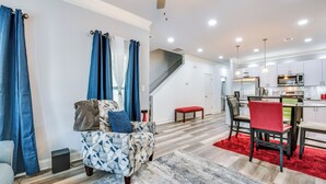 A modern living room with a geometric-patterned sofa, a red ottoman, and a staircase leading to a kitchen area. - Atlanta Home w/ Patio, 8 Mi to Downtown + Aquarium (Atlanta)