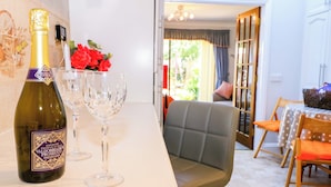 A room with a dining area, a bottle of wine, and two glasses on a counter. - Lavender Cottage (Hailsham)