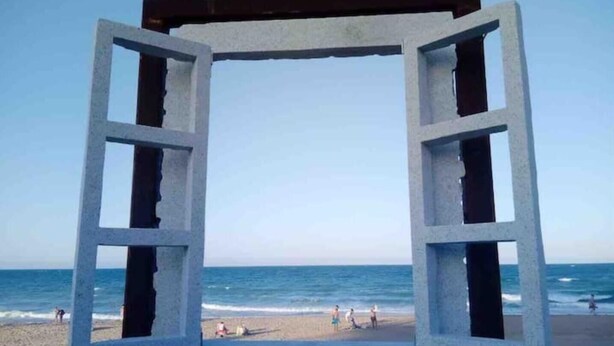 Blick auf den Strand, eingefasst von einer großen, offenen Fensterkonstruktion.