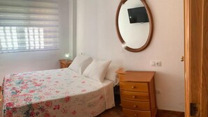 Ein Schlafzimmer mit einem Bett, einem Schminktisch, einem Spiegel und einem Fenster mit Jalousien.